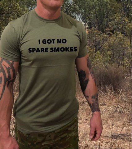 An army defence member standing in the bush whilst deployed on a field exercise with a tshirt that says i got no smokes, to show other people he has no cigarettes to give away