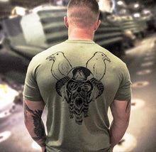 Army soldier facing combat vehicles wearing military green undershirt with a design of Odin and 2 ravens on the back